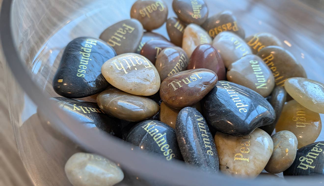 Decorative bowl of engraved stones featuring inspirational words such as “Faith,” “Trust,” “Gratitude,” “Kindness,” and “Peace” used for reflection and support activities