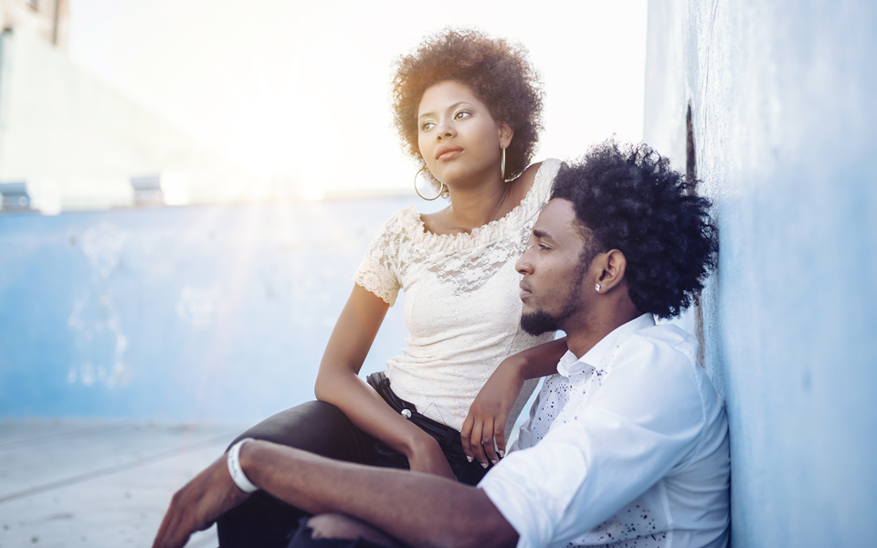 Young couple sitting together outdoors against a blue wall
