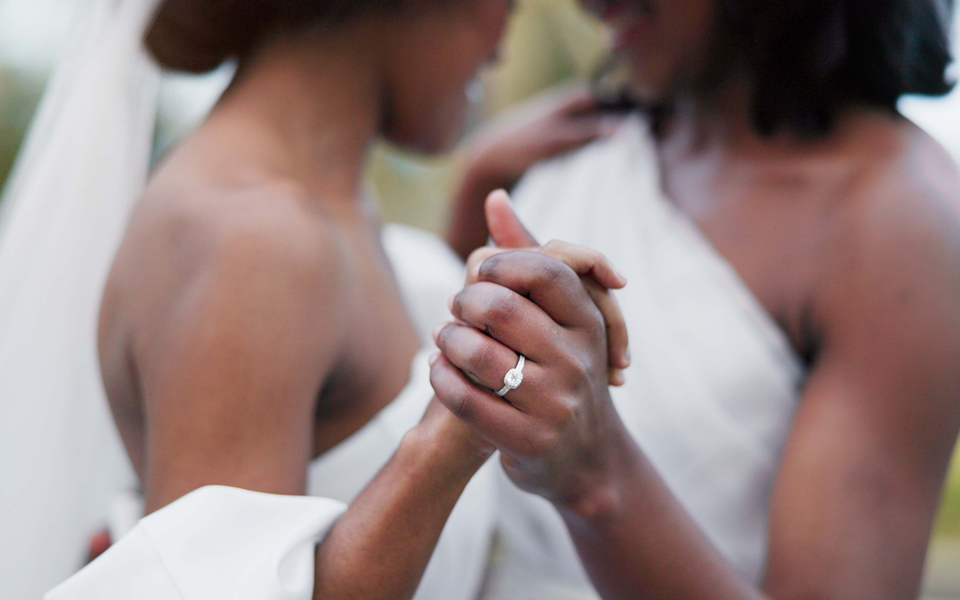 Close-up of two brides holding hands with engagement ring visible