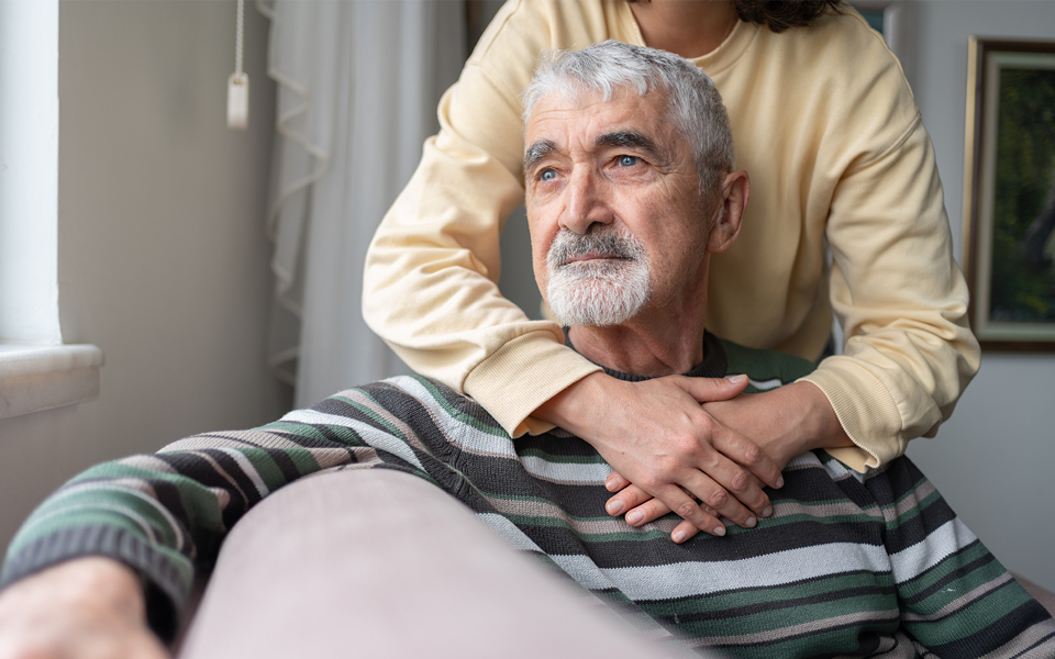 male sitting looking forward with female arms hugging from behind
