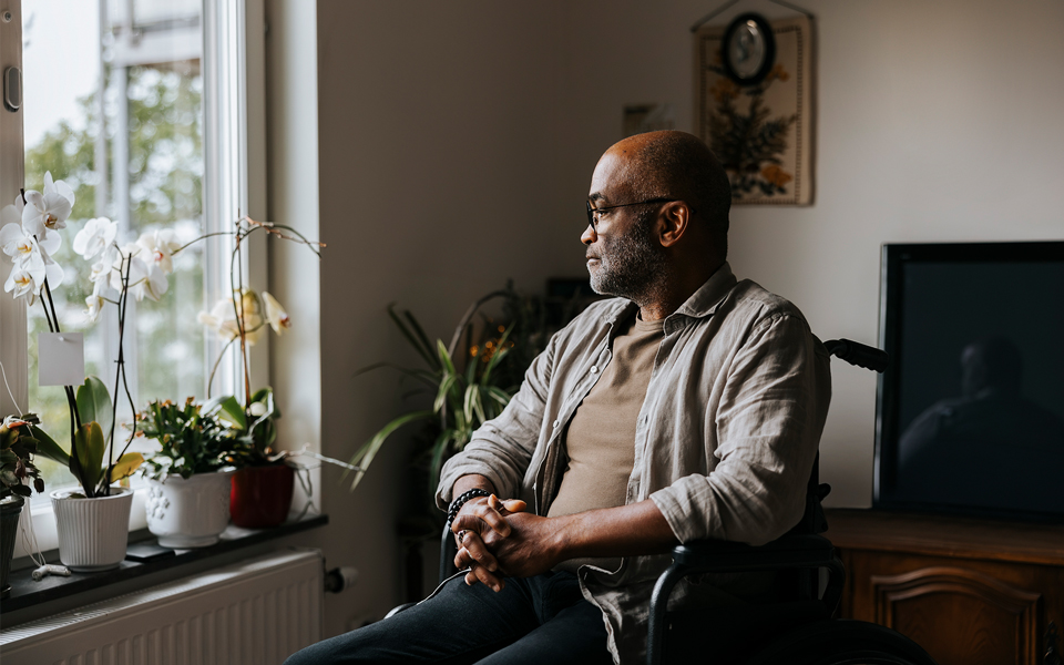 Man sitting thoughtfully in a wheelchair by a window at home