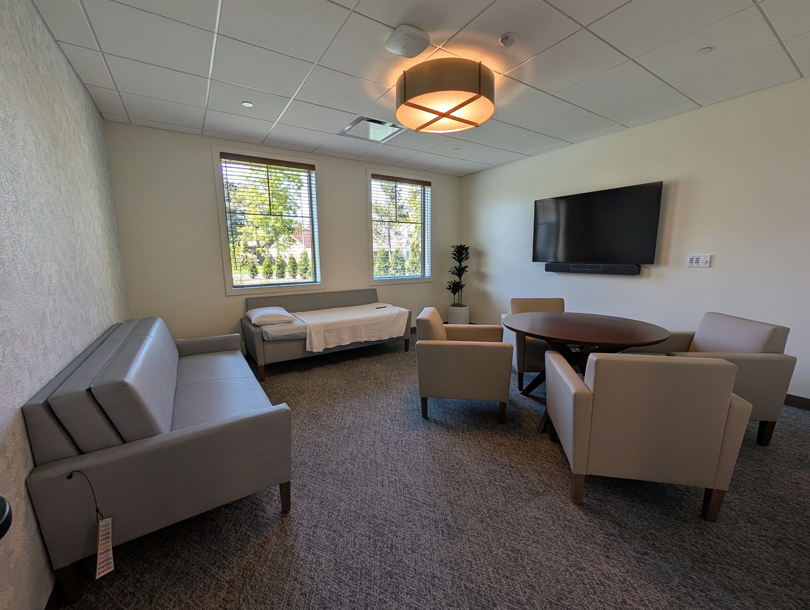 A room with large windows, a table with seating, and several lounge chairs