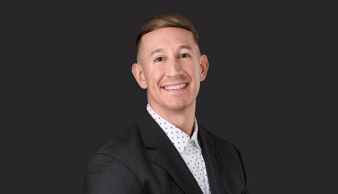 Young businessman in a dark blazer and patterned white shirt smiling in a studio portrait