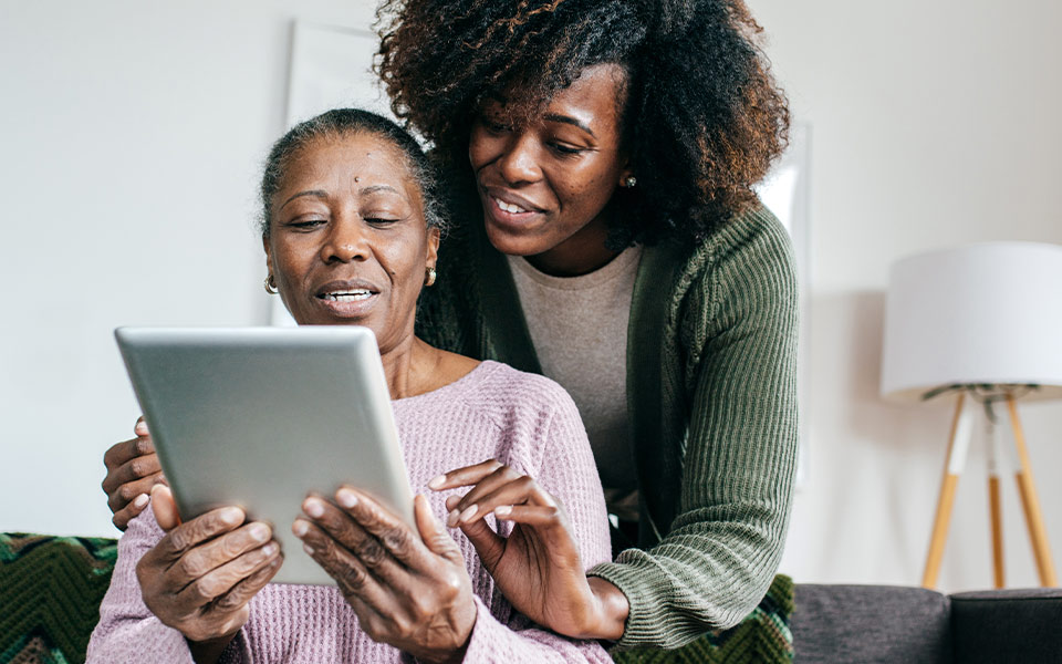 Older woman receiving help using a tablet from a younger caregiver.