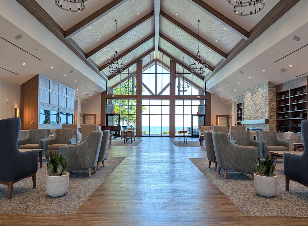 Spacious community gathering lounge with vaulted ceilings, fireplace, and panoramic waterfront windows